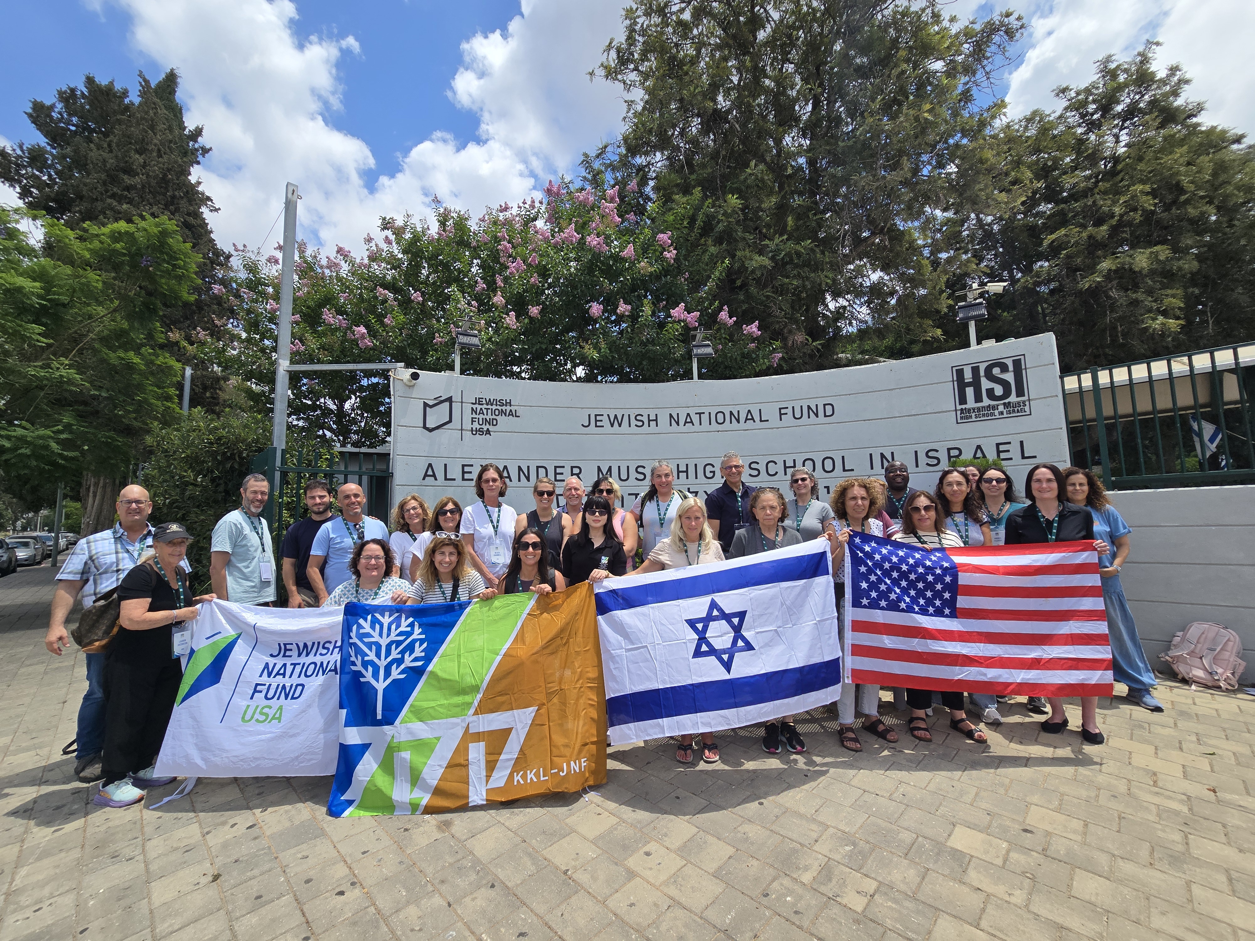 Jewish National Fund-USA's Educators' Mission participants holding flags and posing outside of Alexander Muss High School in Israel