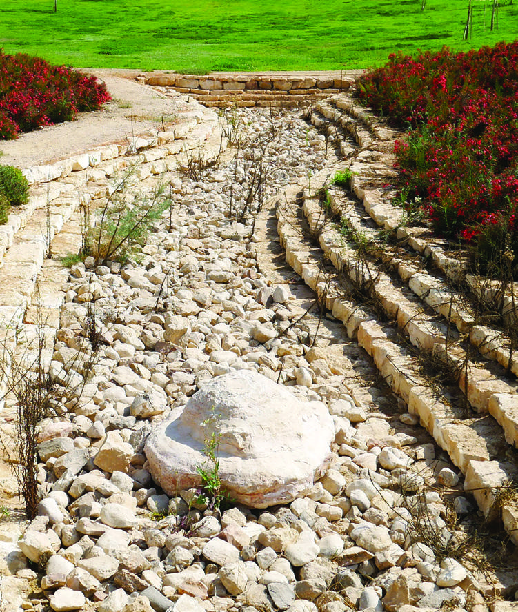 Stone-lined garden channel surrounded by flowers in Arad Park.